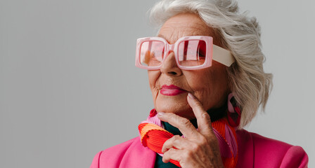 Elegant elderly woman wearing fashionable retro styled eyeglasses and radiating self-love on grey background