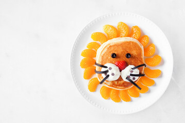 Cute child theme breakfast pancake in the shape of a lion face. Above view on a white marble background. - 765801234