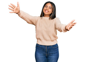 Young latin girl wearing wool winter sweater looking at the camera smiling with open arms for hug. cheerful expression embracing happiness.