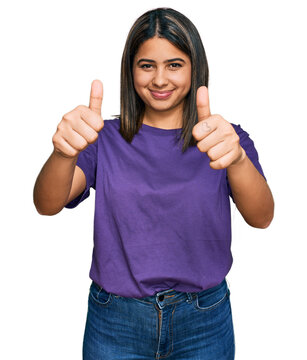 Young hispanic girl wearing casual purple t shirt approving doing positive gesture with hand, thumbs up smiling and happy for success. winner gesture.