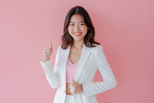 A full-body photo of an Asian woman wearing a white suit and pink top, smiling while showing a thumbs up gesture with one hand on her waist