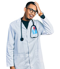 Young african american man wearing doctor uniform and stethoscope surprised with hand on head for mistake, remember error. forgot, bad memory concept.