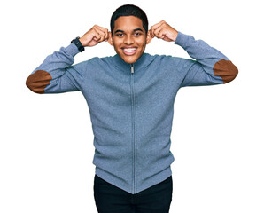 Young handsome hispanic man wearing casual sweatshirt smiling pulling ears with fingers, funny...