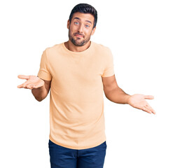 Young hispanic man wearing casual clothes clueless and confused expression with arms and hands...