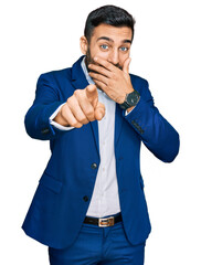 Young hispanic man wearing business jacket laughing at you, pointing finger to the camera with hand...