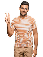 Handsome hispanic man wearing casual clothes smiling looking to the camera showing fingers doing victory sign. number two.