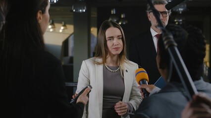 Positive female politician or consul of the European Union answers journalists questions and gives interview for media and television news in government building. Political speech at press conference. - obrazy, fototapety, plakaty