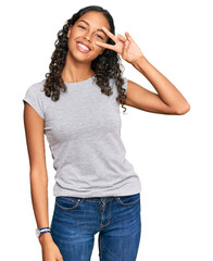 Young african american girl wearing casual clothes doing peace symbol with fingers over face,...