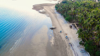 Aerial view of tropical beach with palm trees and boats at low tide