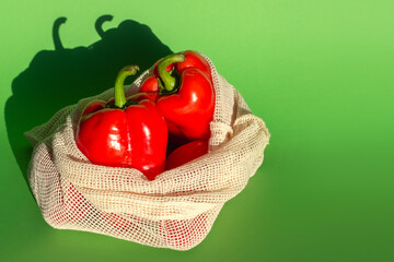 two red sweet peppers in a shopping bag on a green background. flatlay. copy space on the right