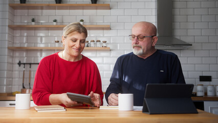 Retired married couple sit in kitchen doing paperwork, checking calculating bills bank loan...