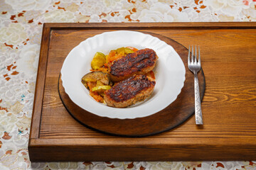 Cutlet with fried vegetables on a white plate on the floor table next to a fork