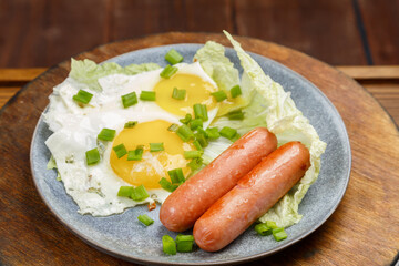 Scrambled eggs of two eggs with sausages sprinkled with green onions on a gray plate on a wooden board