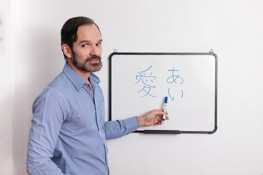 Profesor adulto latino dando clases de japonés en pequeña pizarra acrílica. Indicando si comprendieron la clase