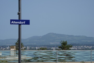 Metal signpost with a blue shield saying name of village Altendorf in Switzerland. Lake Zurich and mountains are on the background. The shield is fixed at the ferry station for personal transport.