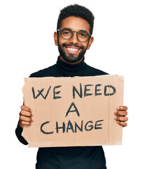 Young african american man holding we need a change banner looking positive and happy standing and smiling with a confident smile showing teeth
