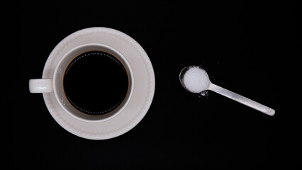 Black coffee and white sugar on a black background. Hot coffee in a white coffee cup with one...