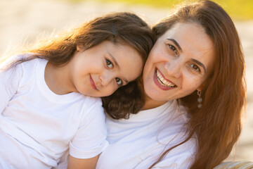 Fototapeta premium Happy mother having fun and hugging with her daughter outdoor - Family and love concept. Portrait of mother and daughter in the city park at summer sunset