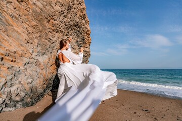 Woman beach white dress flying on Wind. Summer Vacation. A happy woman takes vacation photos to send to friends.