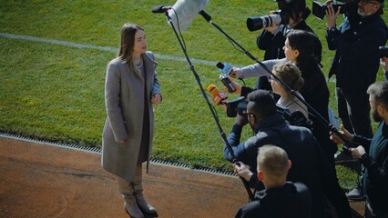 Female director of football team answering press questions and giving interview near soccer field...