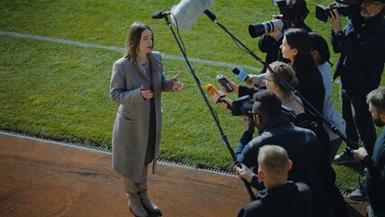 Female director of football team answering press questions and giving interview near soccer field...
