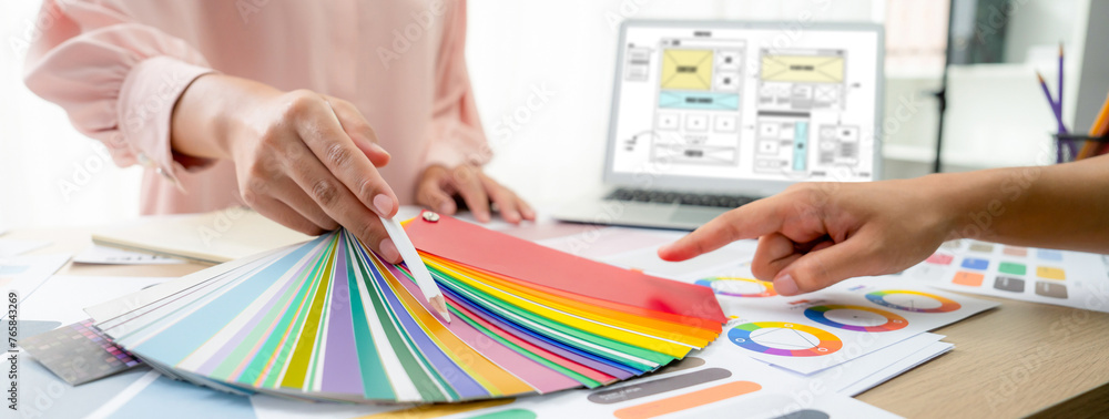 Poster cropped image of interior designer chooses color from color swatches while laptop displayed website 
