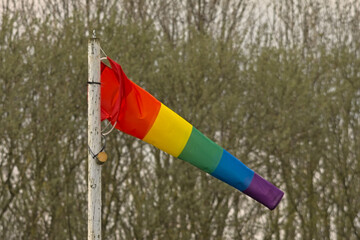 Wind flag with rainbow colors waving, selective focus with bokeh trees in the background 
