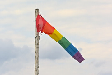 Wind flag with rainbow colors waving on a cloudy sky
