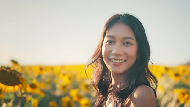 Happy asian woman smiling in sunflower field outdoors, Cheerful Young female looking at the camera feeling free in blooming garden in summer day.