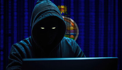 Hacker in a dark hoodie sitting in front of a monitors with Kansas flag and background cyber security concept