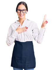 Beautiful brunette young woman wearing professional waitress apron smiling swearing with hand on...