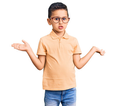 Little cute boy kid wearing casual clothes and glasses clueless and confused expression with arms and hands raised. doubt concept.