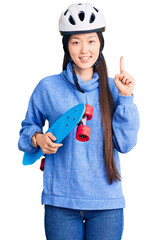 Young beautiful chinese woman wearing security helmet holding skate surprised with an idea or question pointing finger with happy face, number one