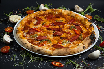 pizza alla diavola with spicy salami, mozzarella, tomato and basil. view from top. black stone...