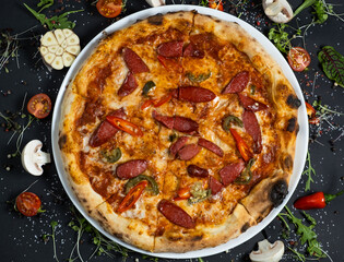 pizza alla diavola with spicy salami, mozzarella, tomato and basil. view from top. black stone background