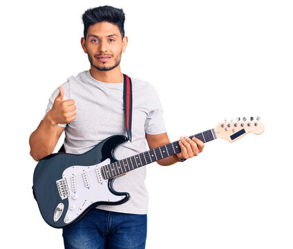Handsome latin american young man playing electric guitar smiling happy and positive, thumb up doing excellent and approval sign