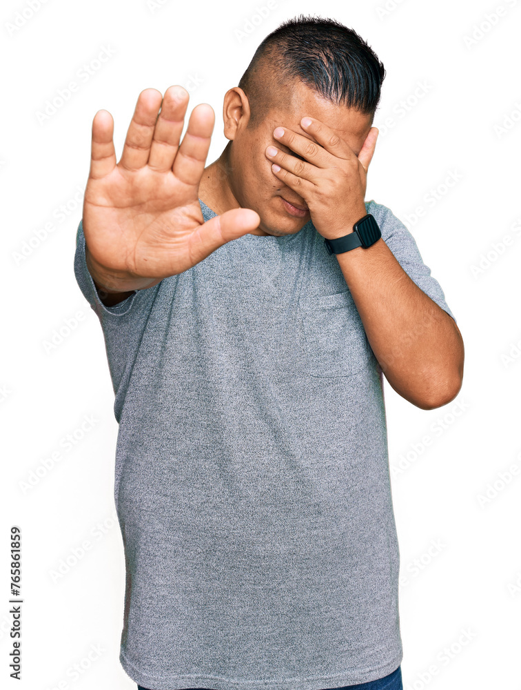 Wall mural young latin man wearing casual clothes covering eyes with hands and doing stop gesture with sad and 