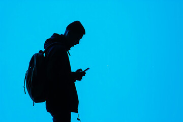 Backlit Silhouette of a Man with Smartphone Against Bright Blue Background