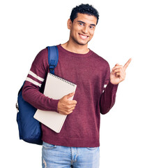 Hispanic handsome young man wearing student backpack and notebook smiling happy pointing with hand...
