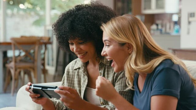 Same Sex Female Couple Or Friends At Home Sitting On Sofa Having Fun Playing Computer Game Together And Giving Each Other High Five - Shot In Slow Motion