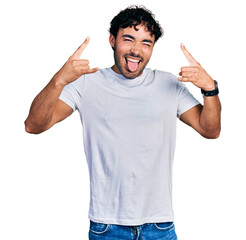 Hispanic young man with beard wearing casual white t shirt shouting with crazy expression doing rock symbol with hands up. music star. heavy music concept.