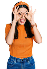 Obraz na płótnie Canvas Young hispanic woman wearing casual clothes doing ok gesture like binoculars sticking tongue out, eyes looking through fingers. crazy expression.