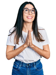 Young hispanic woman wearing casual clothes and glasses begging and praying with hands together...