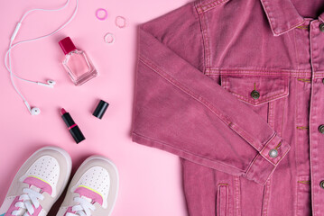 Pink denim jacket with cosmetics on pink background. Top view point, flat lay.