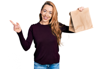Young caucasian woman holding take away paper bag smiling happy pointing with hand and finger to the side