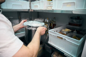 Chef putting dish in saucepan on shelf in refrigerator storage in restaurant