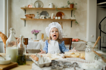 Girl cook 3 years old in a beautiful kitchen, in a chef's hat, in an apron, daylight