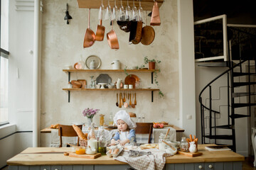 Girl cook 3 years old in a beautiful kitchen, in a chef's hat, in an apron, daylight