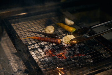 Vegetables of onions and carrots frying on iron net in burning fire place