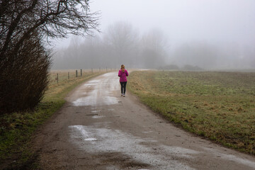 Obraz premium Natural landscape of a foggy morning in the countryside and an athletic woman runs along the road in sportswear.